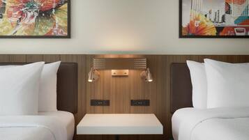 Habitación de hotel con dos camas, una mesa en el centro y obras de arte en las paredes.