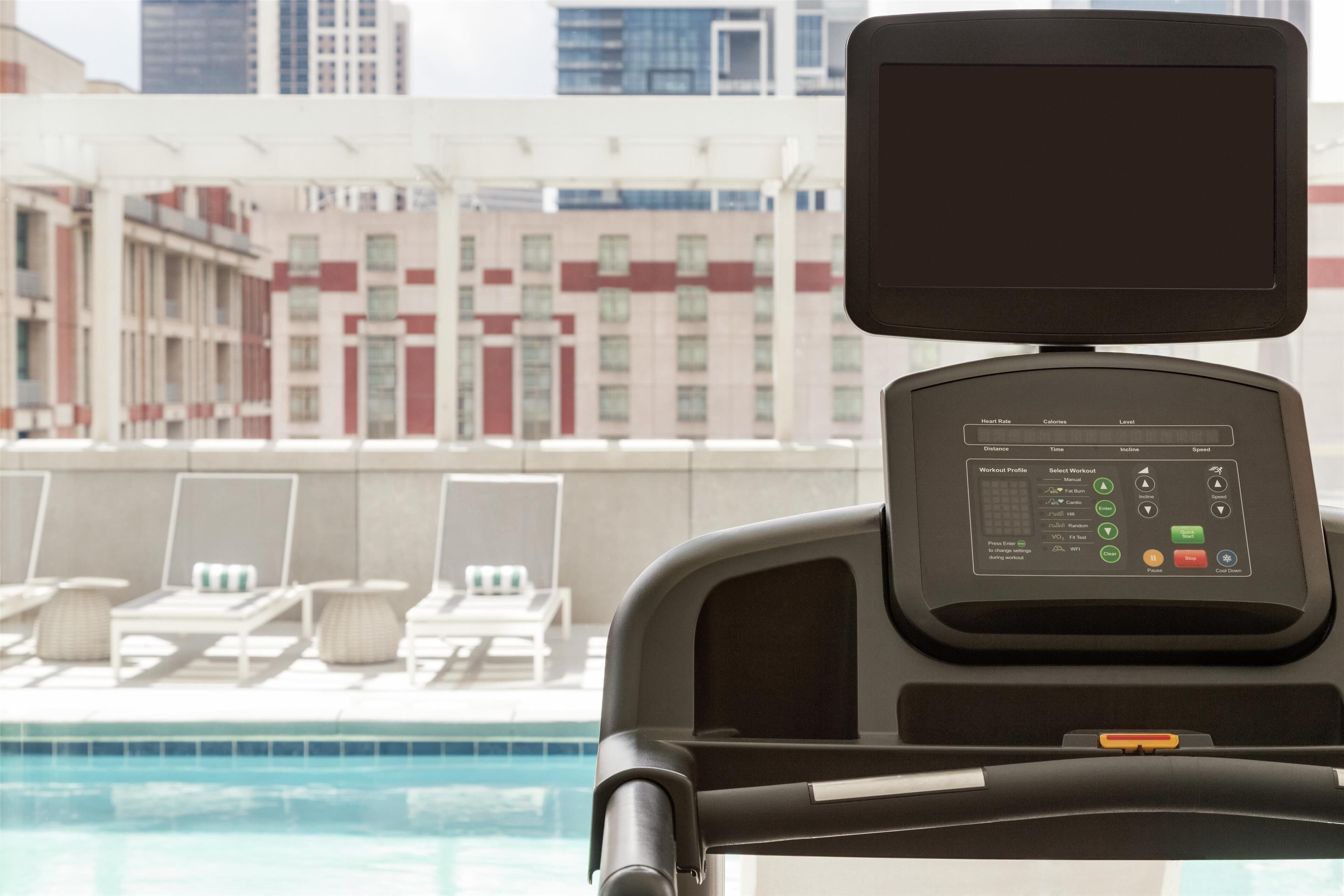 A stationary bike with a digital display, a poolside lounge area, and a cityscape view.
