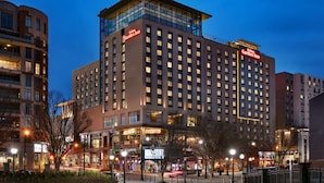Un hotel de varios pisos con un llamativo letrero de "Hilton Garden Inn", que presenta un diseño arquitectónico moderno con grandes ventanales y un techo plano.
