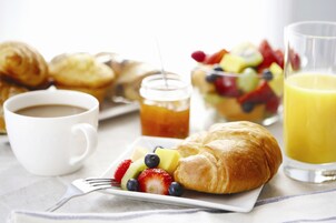Desayuno con cruasanes, fruta, café y jugo de naranja.