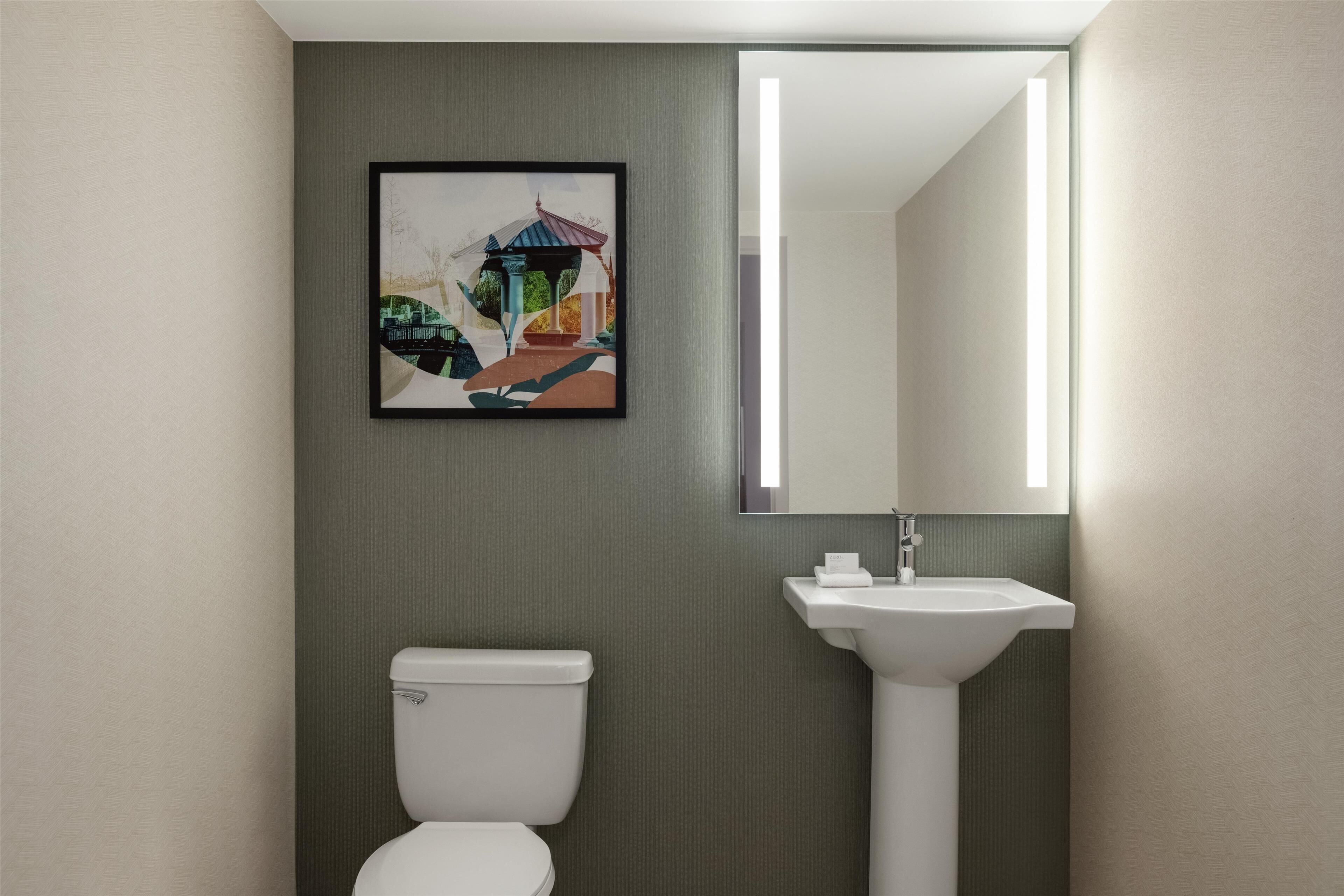 A bathroom with a toilet, sink, and a framed picture on the wall.
