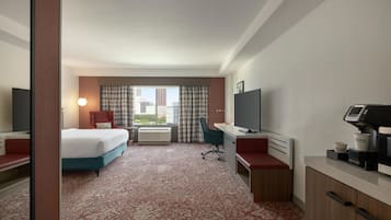 Quarto de hotel com cama, escrivaninha, cadeira, televisão e vista para a cidade.