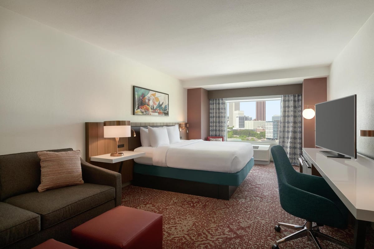 Habitación de hotel con cama, escritorio, televisión, sofá y ventana con vistas a la ciudad.