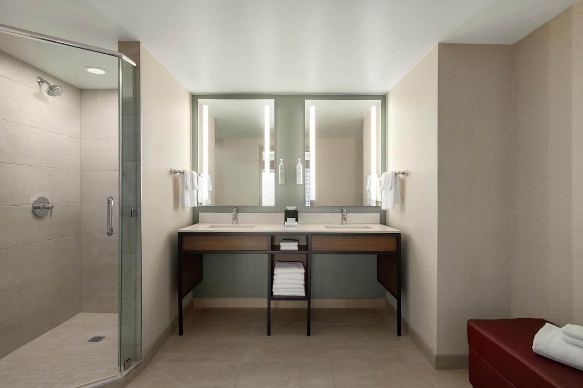 Un baño moderno con cabina de ducha de vidrio, lavamanos dobles y tocador con toallero.