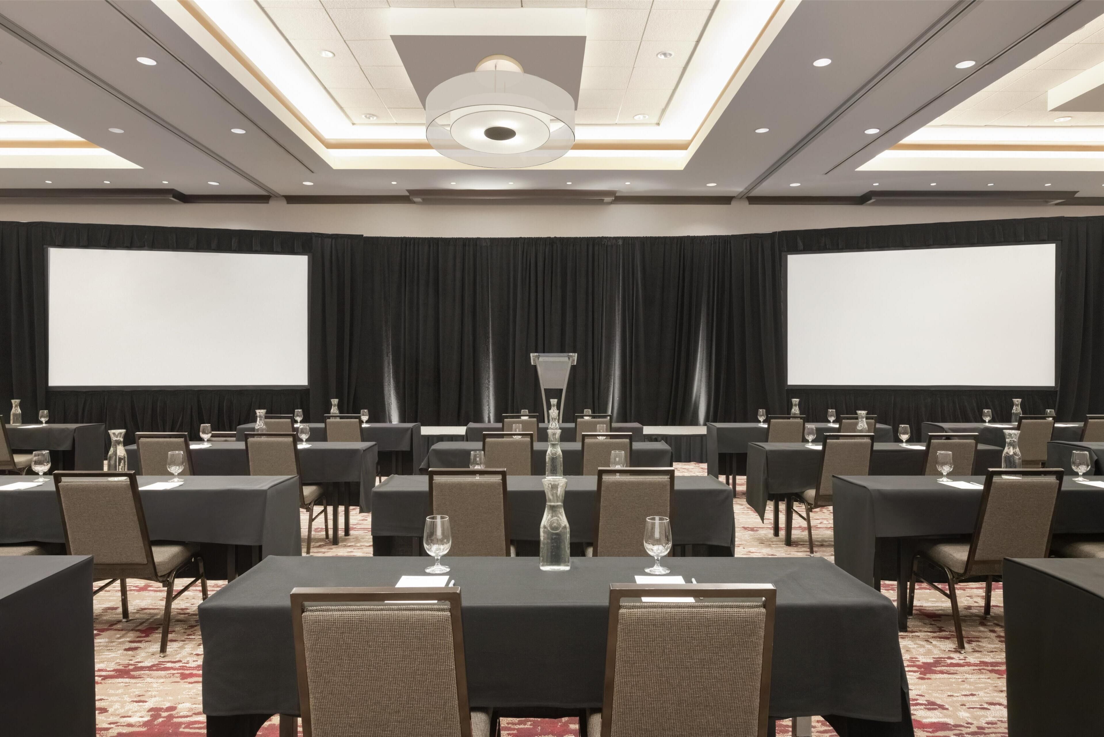 A conference room with tables, chairs, a projector screen, and a large screen.