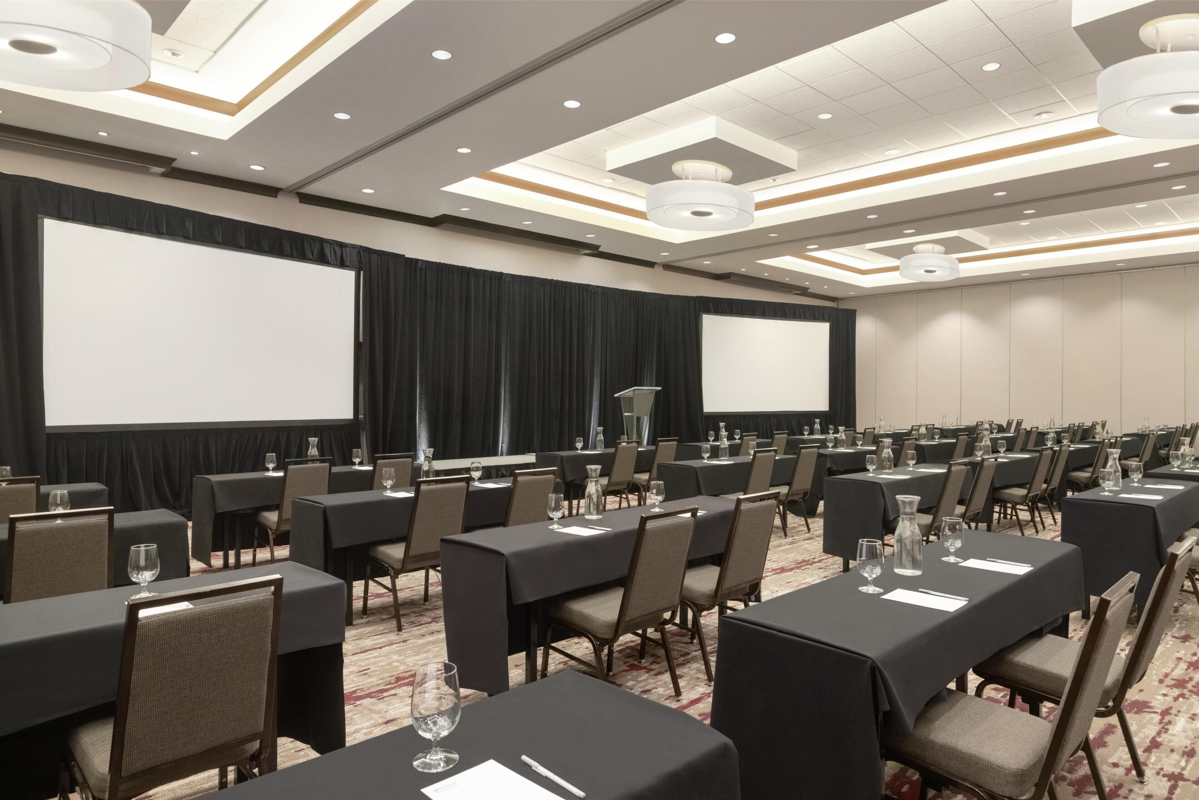 A conference room with multiple tables, chairs, a projector screen, and a large screen.