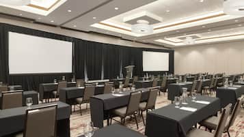 A conference room with multiple tables, chairs, a projector screen, and a large screen.