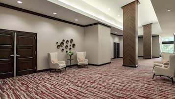 A spacious lobby with a red and white patterned carpet, two white armchairs, a small table with a vase, and a wall-mounted circular decoration.