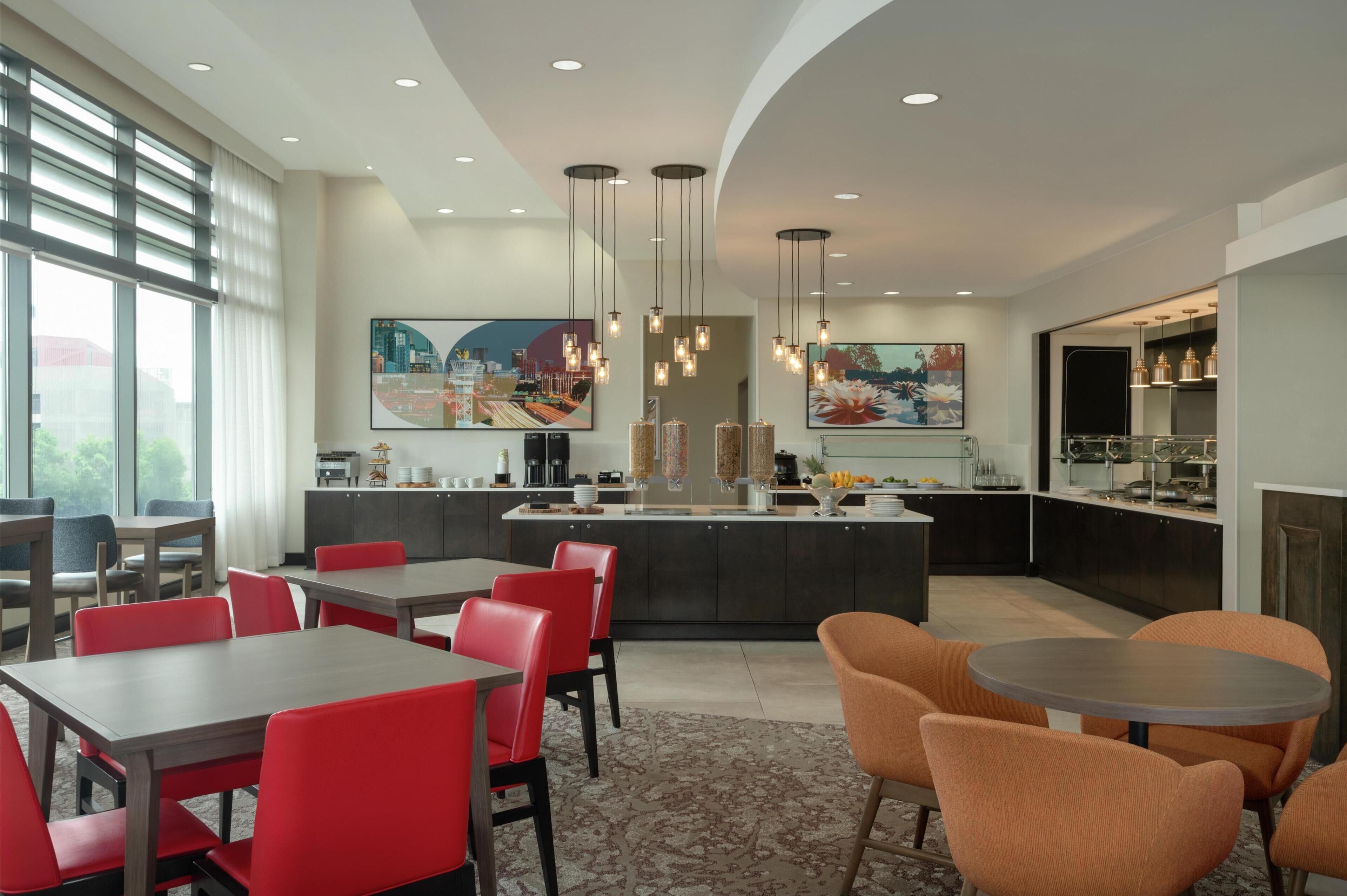 A modern hotel lobby with a dining area, kitchen, and artwork.
