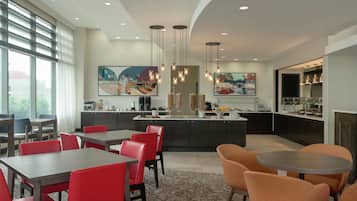 A modern hotel lobby with a dining area, kitchen, and artwork.