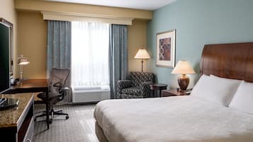 Habitación de hotel con cama, escritorio, silla, dos lámparas y una ventana con cortinas.