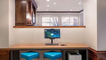A modern office with a wooden desk, two blue cushioned stools, a computer monitor, and a printer.