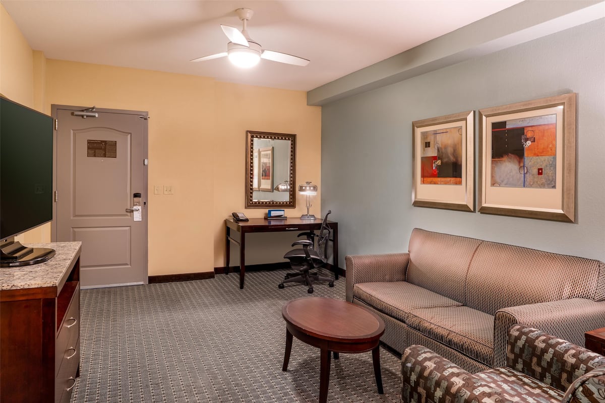 A hotel room with a desk, office chair, sofa, and a small table.