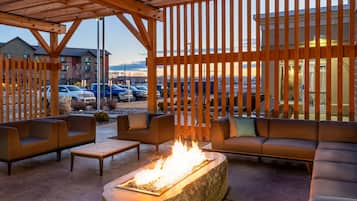 An outdoor seating area with a fire feature, wooden pergola, and a view of a parking lot and buildings.