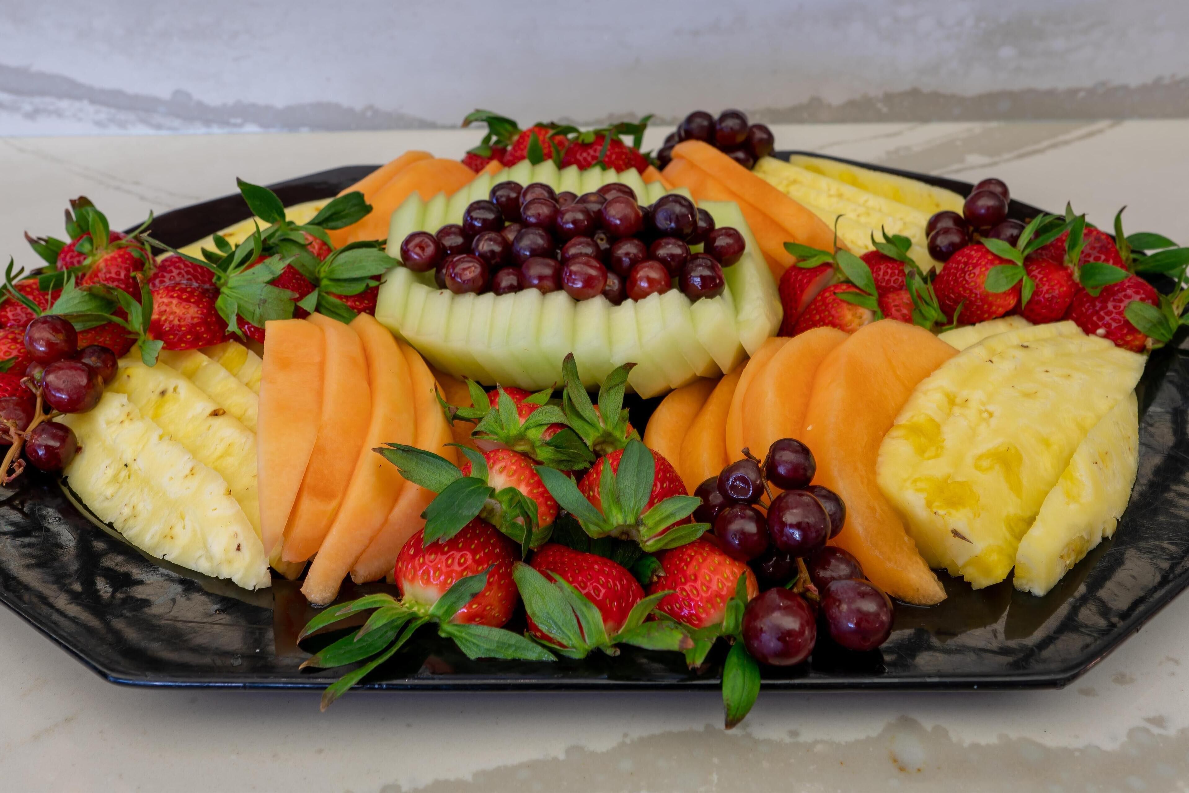 Una bandeja de frutas con fresas, uvas, piña y melón cantalupo.