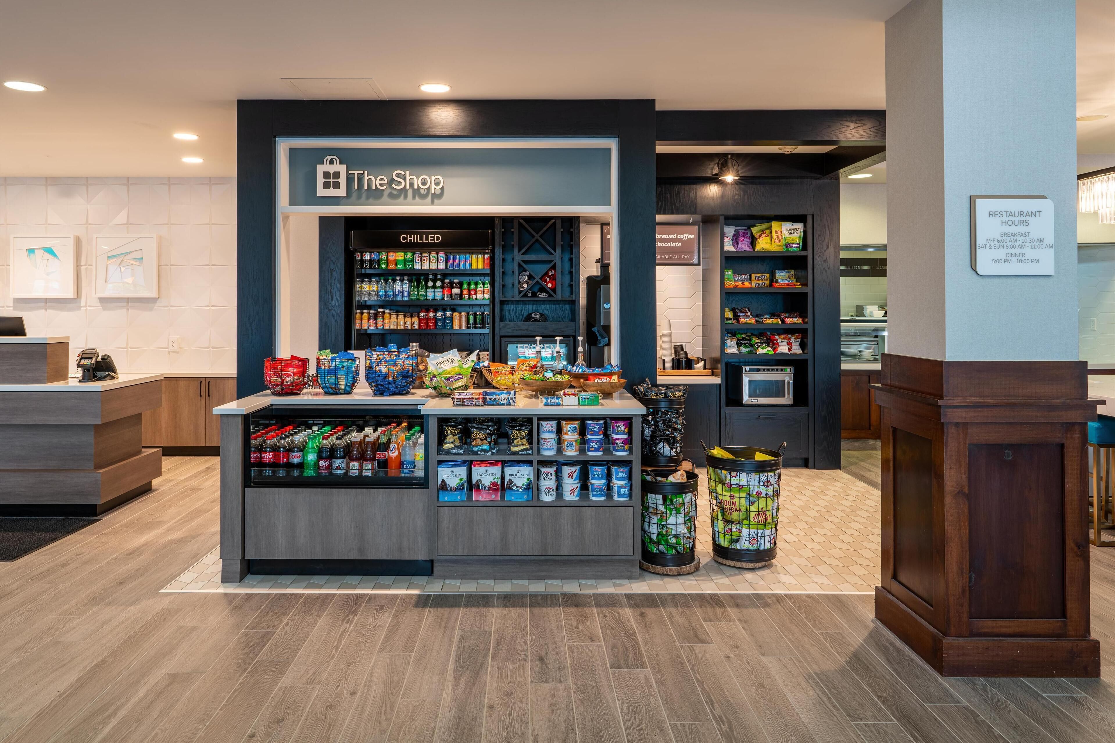 A retail area with a 'The Shop' sign, refrigerated section, snack and beverage displays, and a trash can.