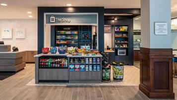 A retail area with a 'The Shop' sign, refrigerated section, snack and beverage displays, and a trash can.
