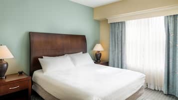A hotel room with a large bed, two bedside tables with lamps, a window with curtains, and a headboard.