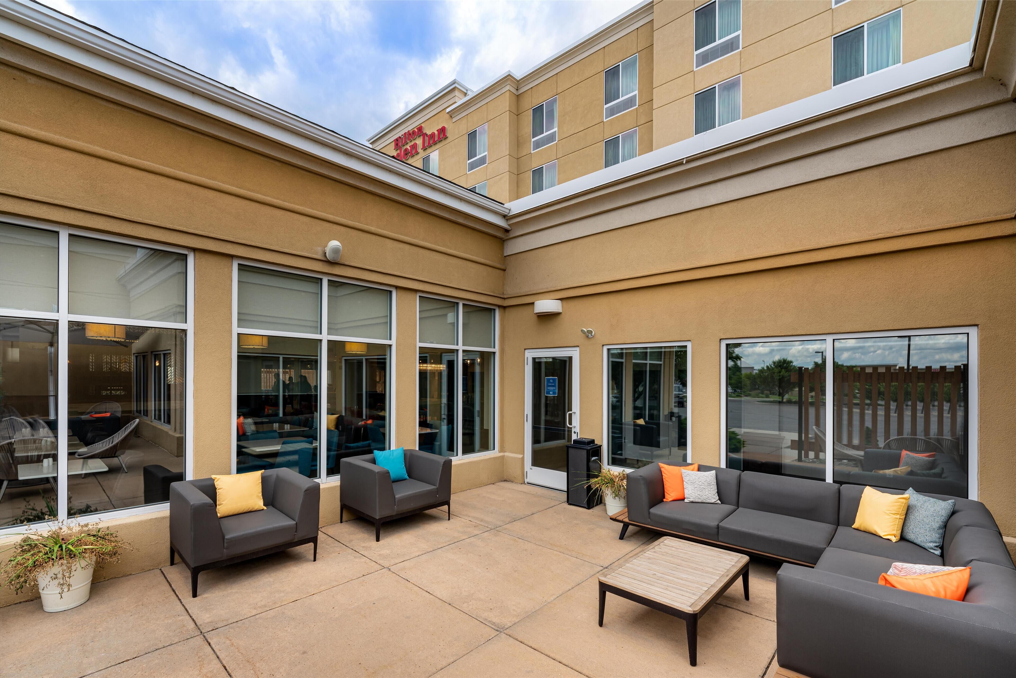 A hotel courtyard with outdoor seating, large windows, and a sign above the entrance.