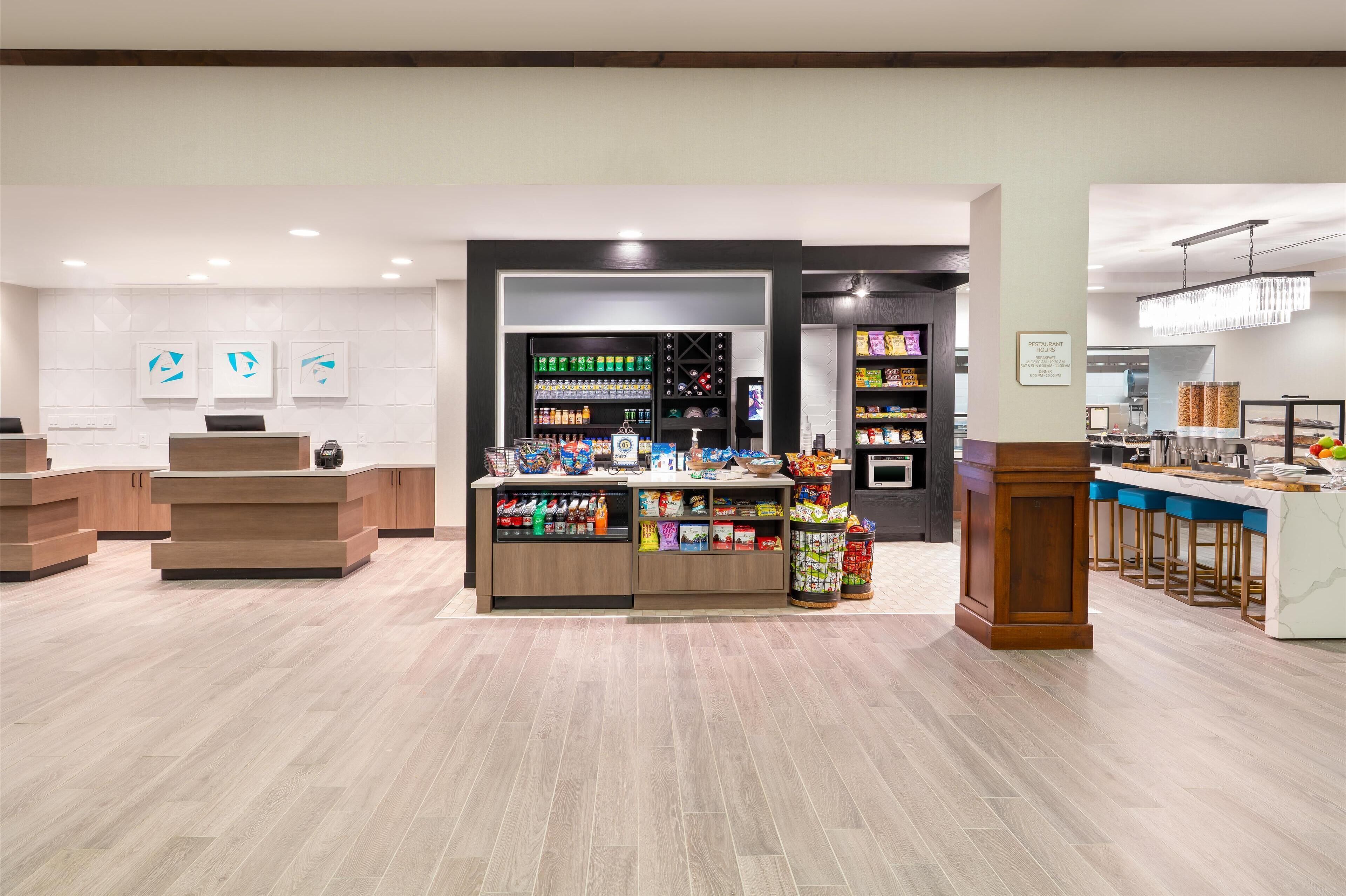 A modern hotel lobby with a reception desk, a beverage kiosk, and a bar area.