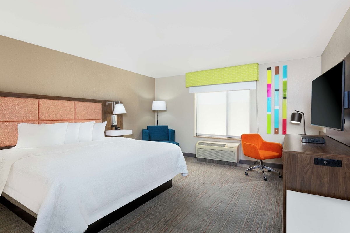 Una habitación de hotel con cama, escritorio, televisión y ventana con persianas.