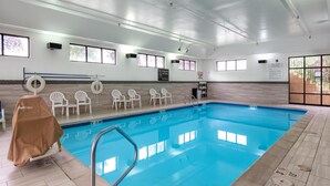An indoor swimming pool with clear blue water, surrounded by white chairs and a covered chair.