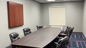 Un salón de conferencias con una larga mesa, seis sillas, una pantalla de proyector y un armario de madera.
