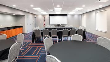 Un salón de conferencias con una gran mesa, varias sillas, una pantalla de proyector y piso alfombrado.