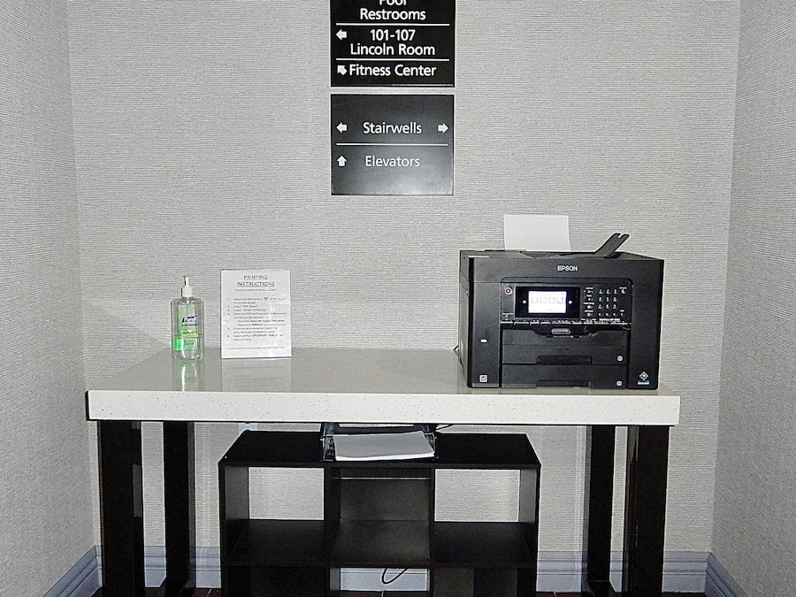 Quarto de hotel com uma mesa, uma impressora e um aviso indicando serviços e comodidades para hóspedes.