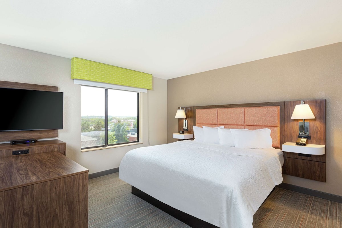 Habitación de hotel con cama, televisor, ventana y vista a la ciudad.