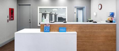 A hotel reception desk with a modern design, a clock on the wall, and a welcome mat at the entrance.