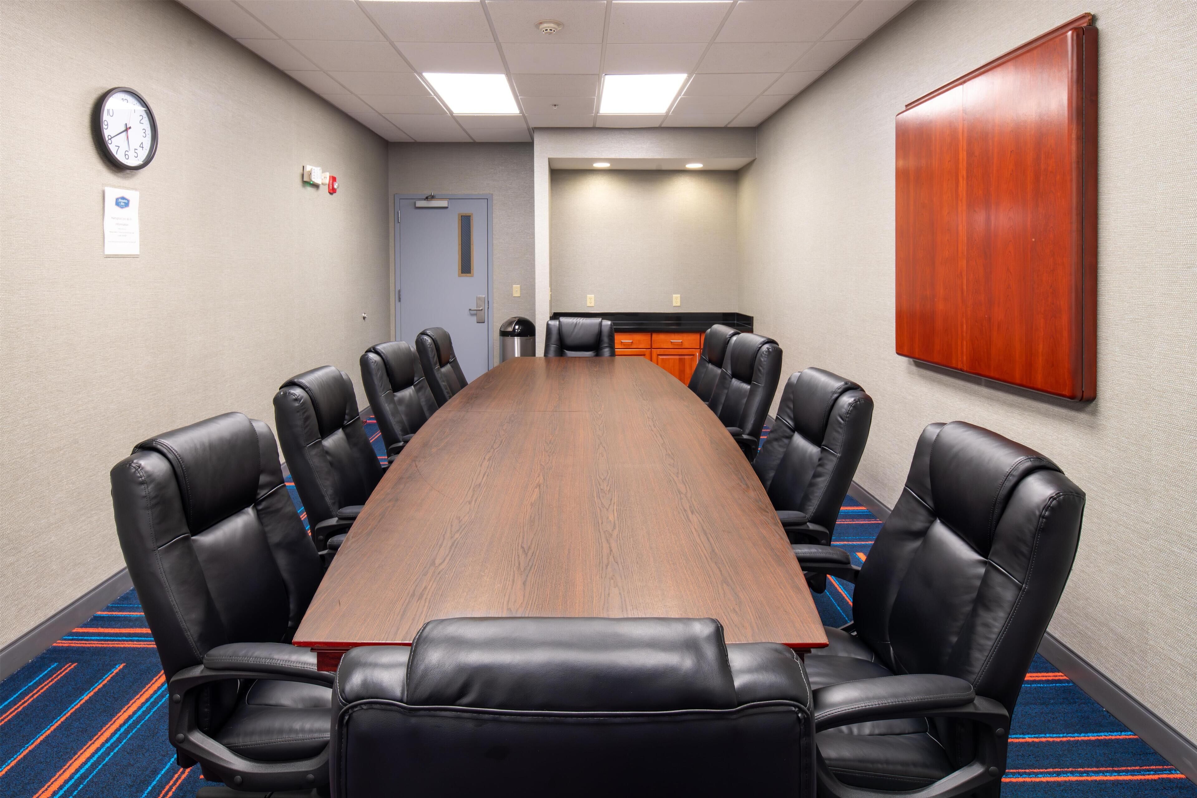 A conference room with a long wooden table and black leather chairs.