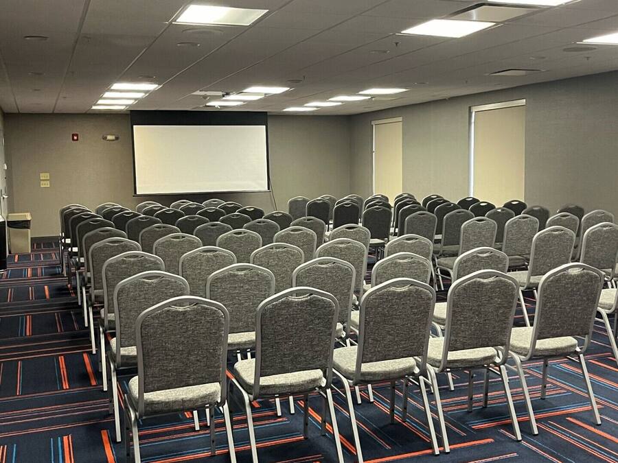 A conference room with rows of chairs, a projector screen, and carpeted flooring.
