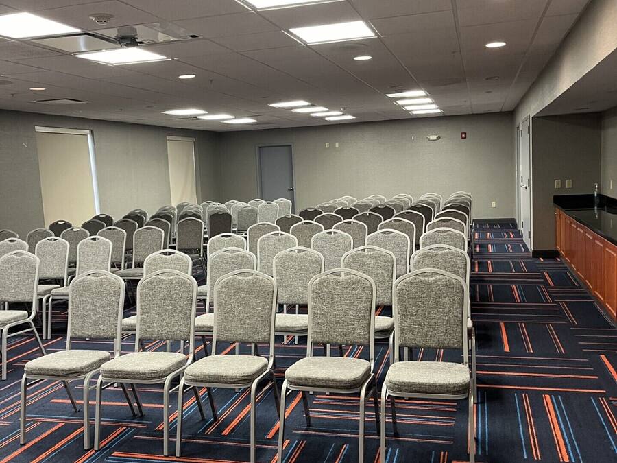 Une salle de conférence avec des rangées de chaises, un sol recouvert de moquette et des luminaires au plafond.