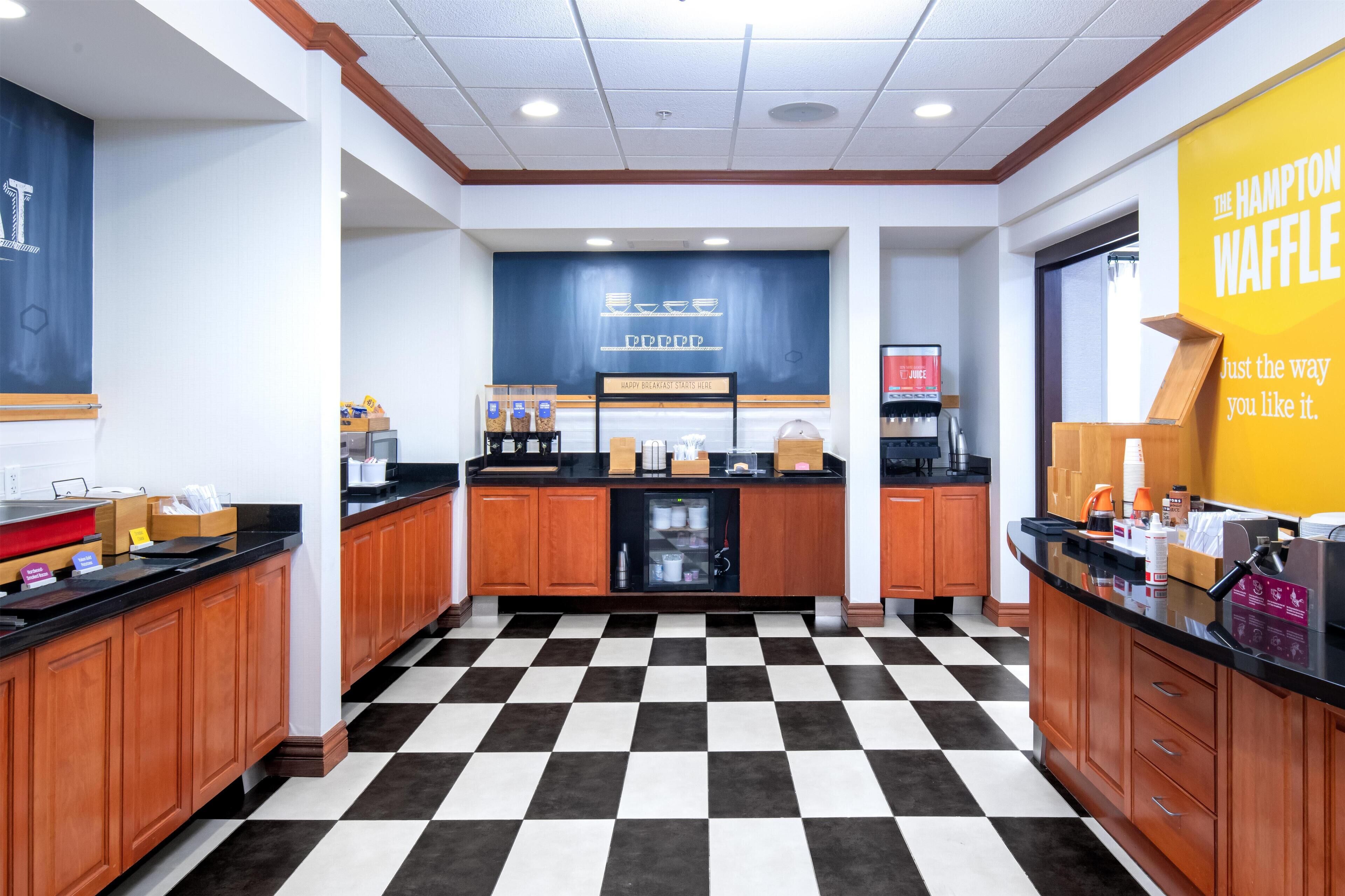 Una zona de cocina con suelo a cuadros, armarios de madera, una cafetera y un cartel que dice The Hampton Waffle.