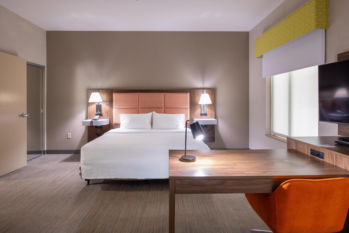 Una habitación de hotel con una cama grande, dos lámparas de noche, un escritorio con una silla y un televisor.