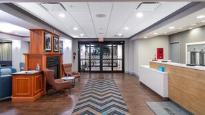 A hotel lobby with a reception desk, a fireplace, seating area, and a patterned rug.