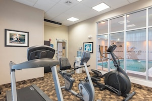 Un gimnasio con cintas de correr, elíptica y bicicleta estática, con una piscina visible a través de la ventana.