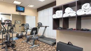 A gym with exercise equipment, a television, and a shelf with towels.
