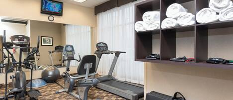 A gym with exercise equipment, a television, and a shelf with towels.