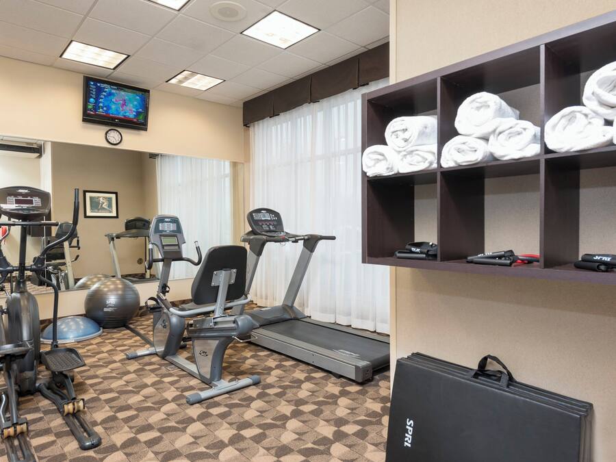 A gym with exercise equipment, a television, and a shelf with towels.