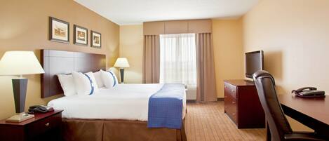 A hotel room with a large bed, two bedside lamps, a desk with a telephone, and a television.