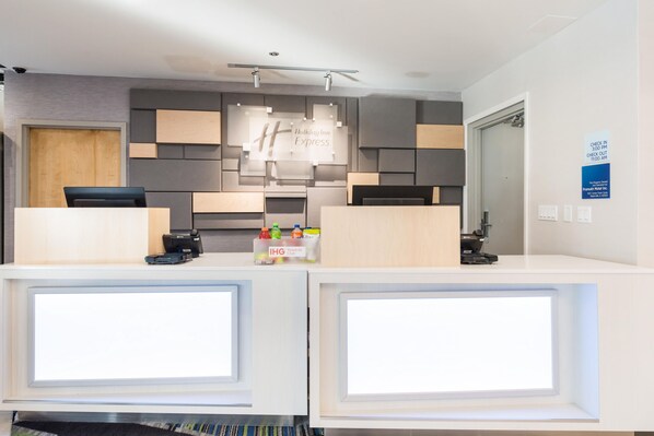 A hotel reception desk with a modern design, including a check-in/check-out sign, a Holiday Inn Express logo, and a rewards club sign. - Holiday Inn Aurora North - Naperville by IHG (Aurora)