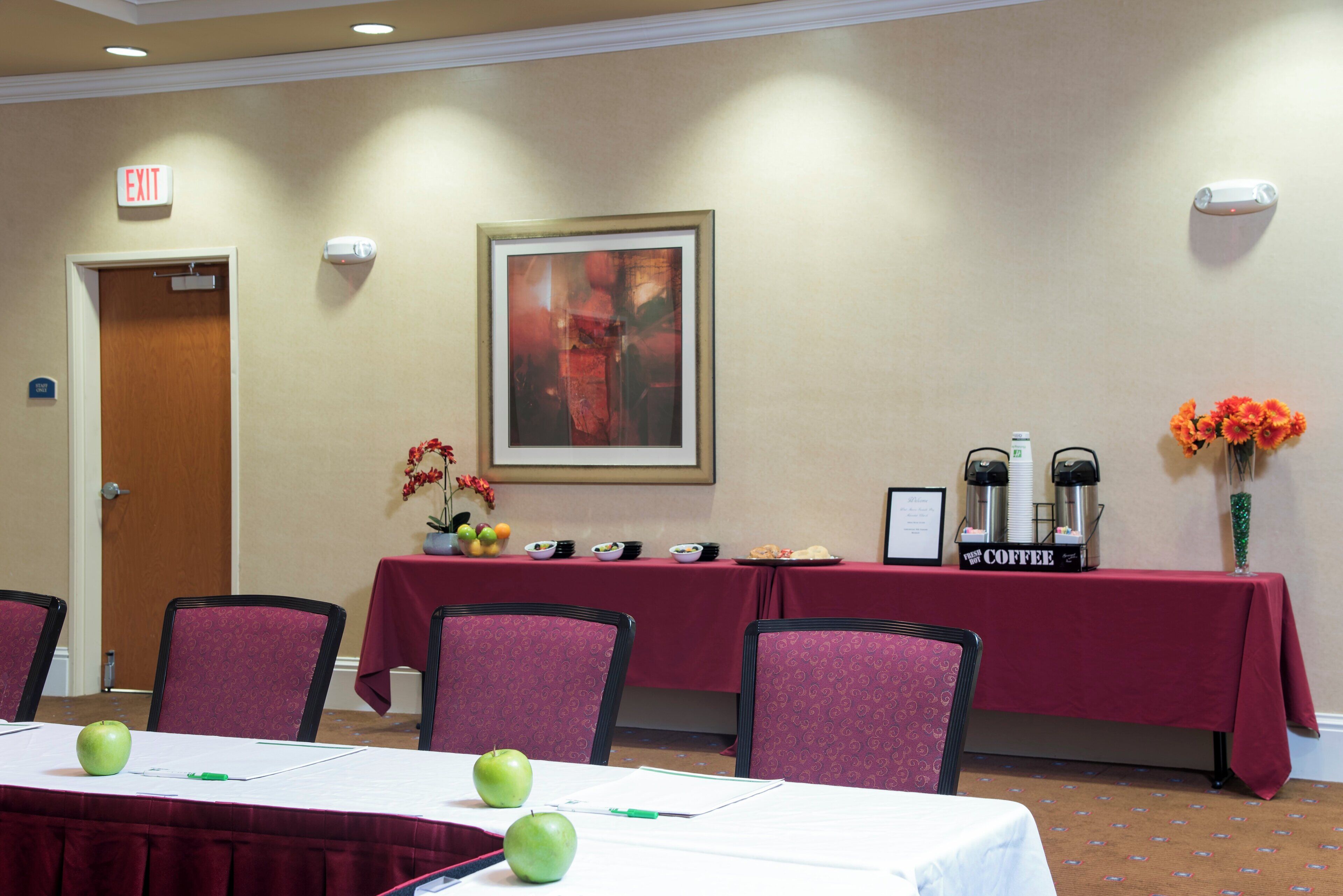 Un salón de conferencias con una mesa dispuesta para una reunión, sillas, una estación de café y un letrero de salida.