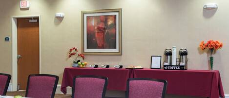 A conference room with a table set for a meeting, chairs, a coffee station, and an exit sign.