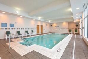 Une piscine intérieure avec un sol carrelé, un escalier pour entrer dans la piscine et plusieurs chaises le long du mur.