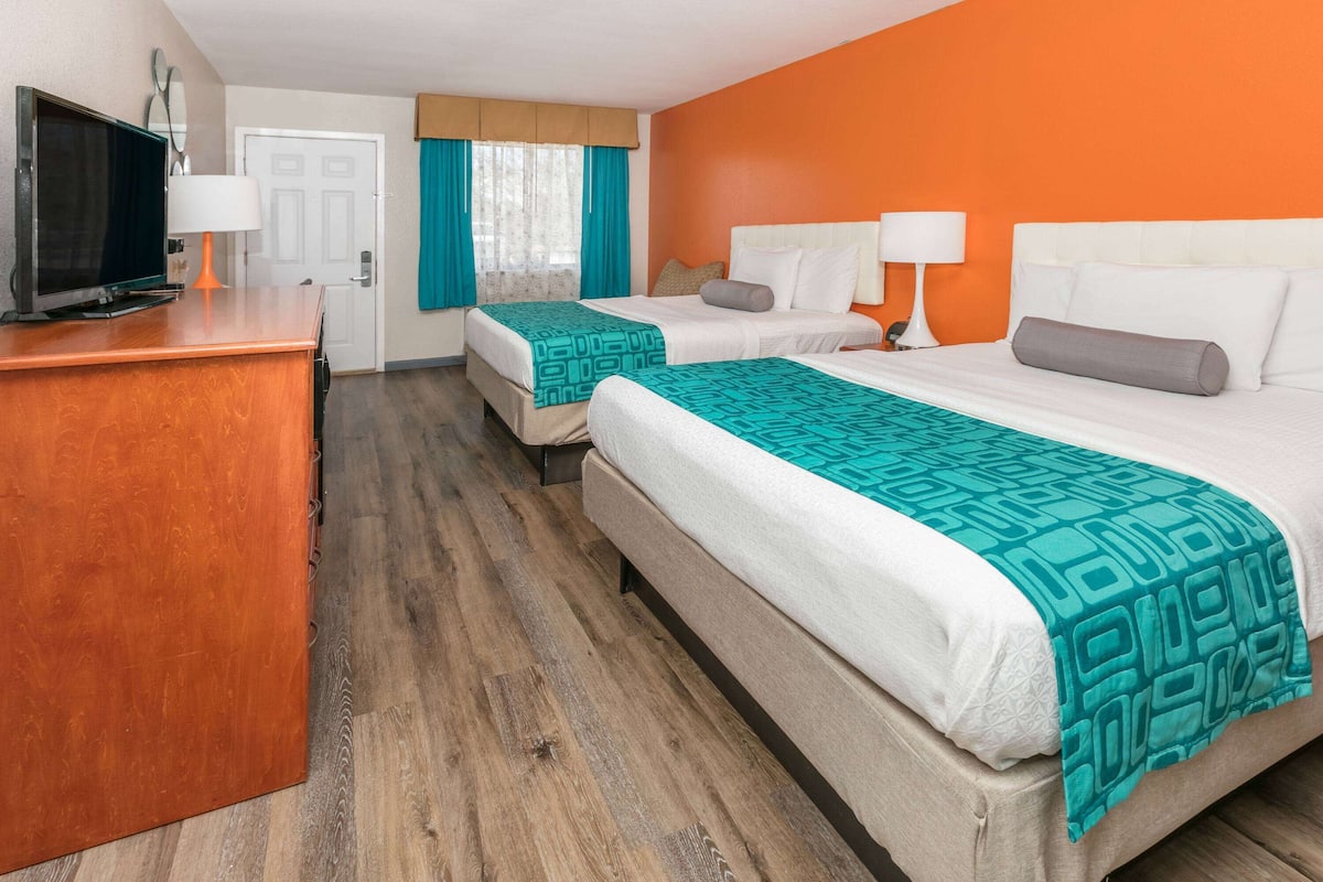 A hotel room with two beds, a TV, and a wooden dresser.