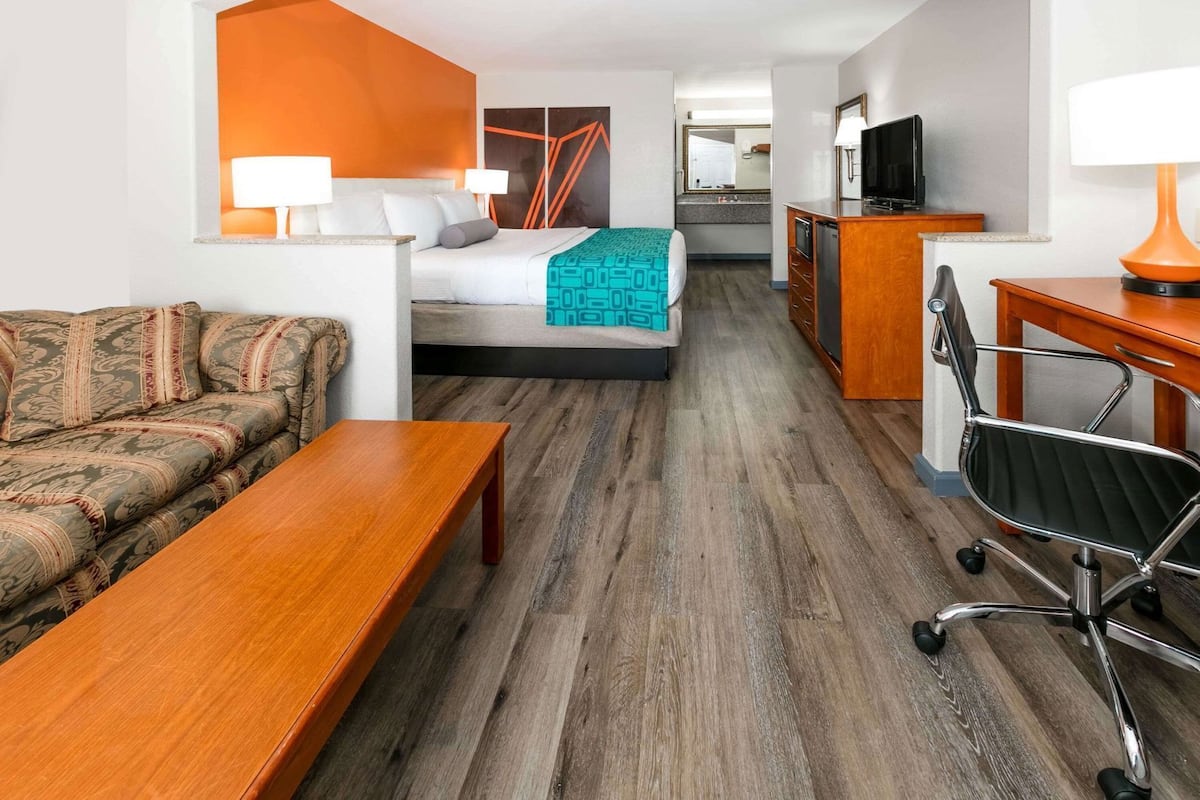 A hotel room with a sofa, a bed with a teal blanket, a desk with a lamp, a chair, and a TV.