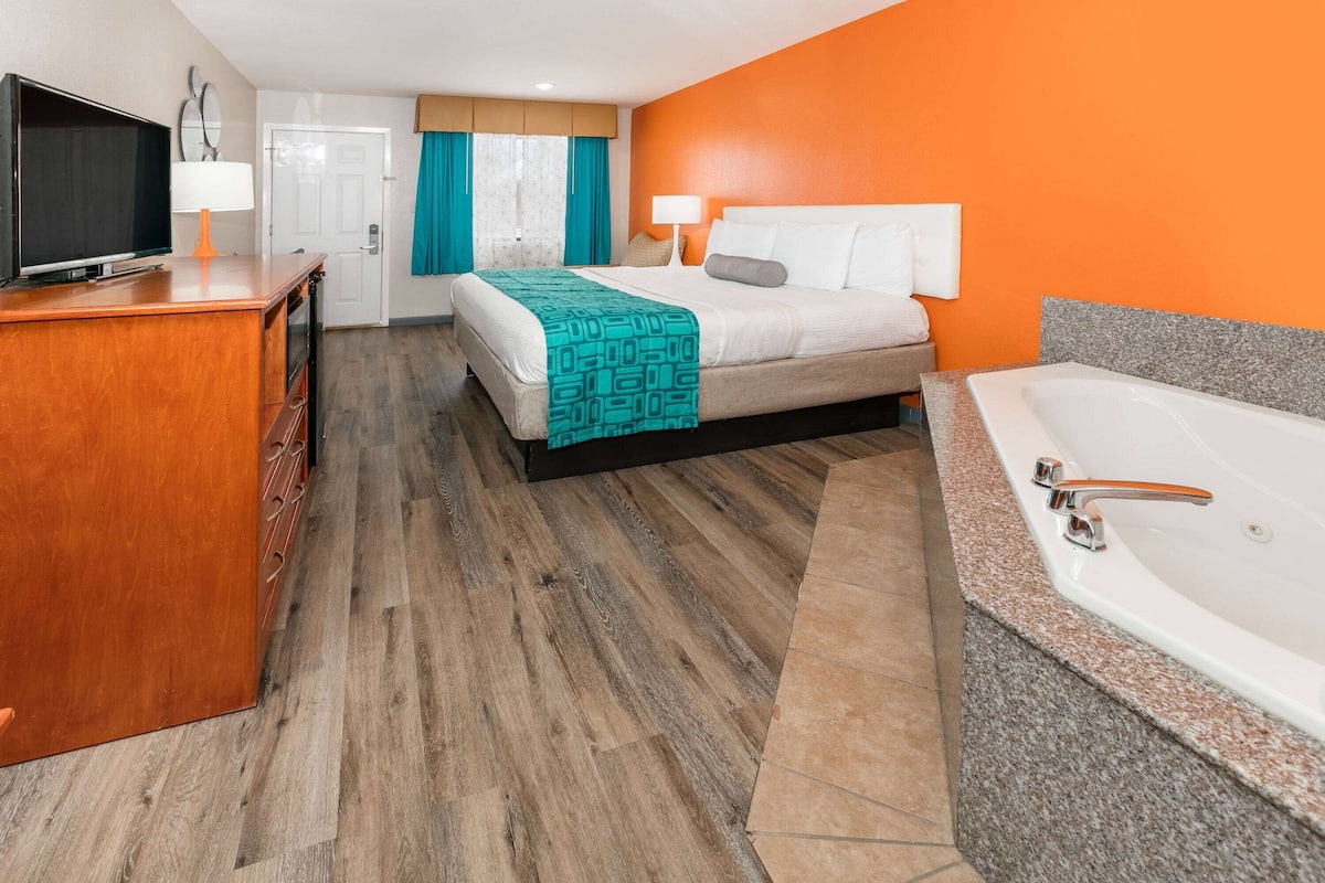 A hotel room with a bed, a TV, a desk, a bathroom with a bathtub, and a door.