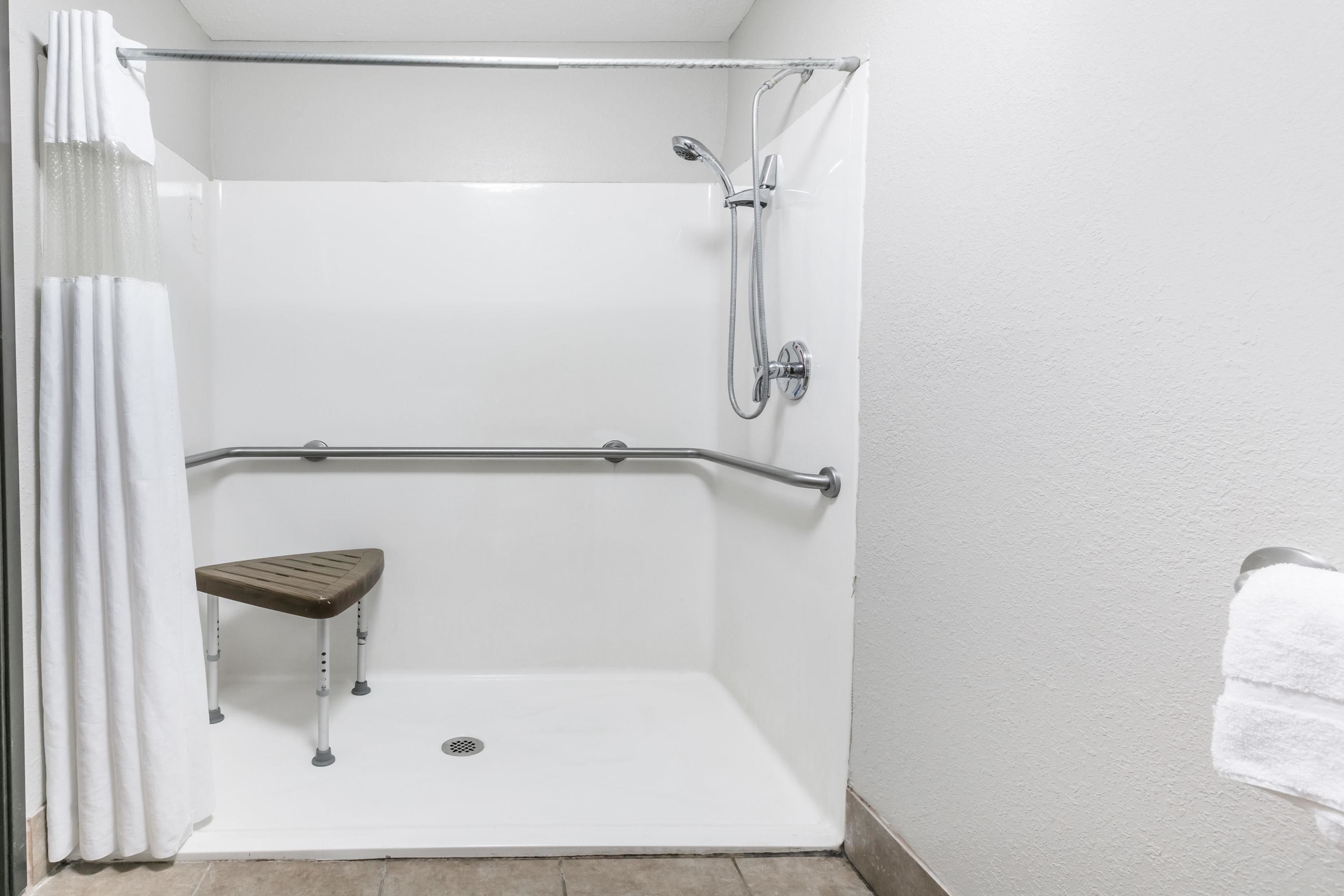 A walk-in shower with a bench, grab bars, and a showerhead.